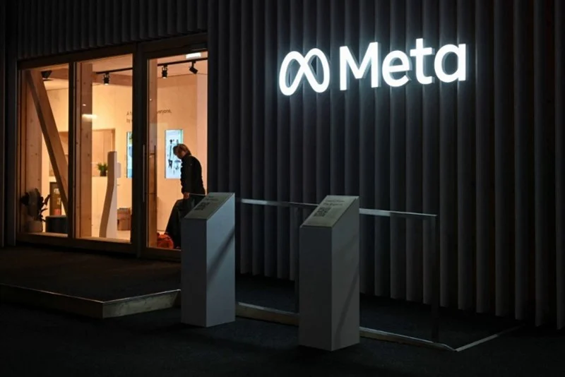 Night view of the Meta office entrance with the glowing Meta logo on a dark exterior and a person entering through glass doors.