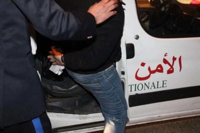 Two men stand near a white van with red Arabic text, one helping the other into the vehicle at night.
