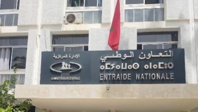 Facade of a government building with a sign reading ENTRAIDE NATIONALE in French and Arabic text, and a red flag above the entrance.
