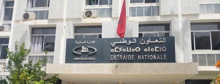 Facade of a government building with a sign reading ENTRAIDE NATIONALE in French and Arabic text, and a red flag above the entrance.