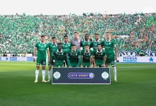 Soccer team in green jerseys posing for a group photo on the field with a banner reading COTE-SPORT and a packed green-clad stadium behind them **(informative image).