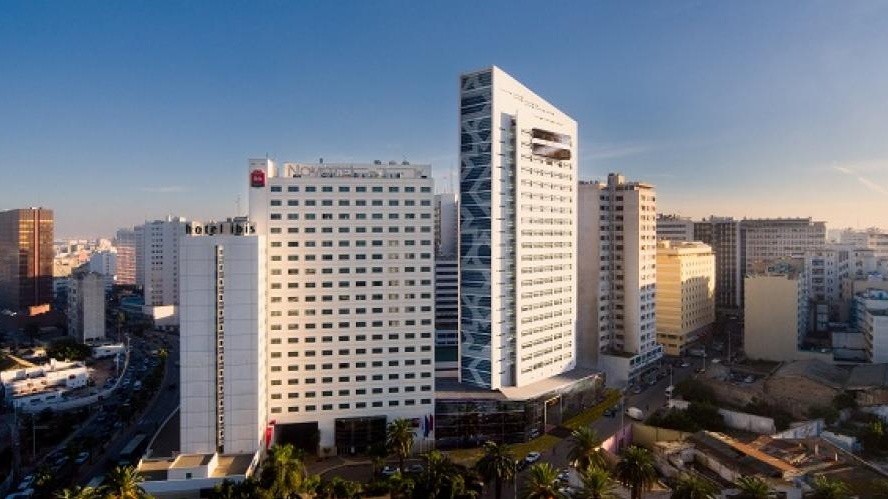 City skyline with modern white office towers and palm trees in the foreground at clear weather, blue sky above.