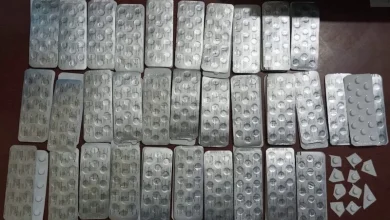 Numerous silver blister packs with round white pills laid out in rows on a dark wooden table.
