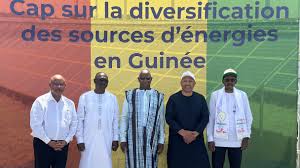 Five men pose in front of a colorful banner promoting energy diversification in Guinea.