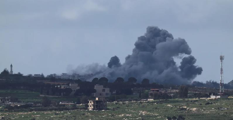 Large black smoke plume rising over a town from an explosion, with scattered buildings and open fields in the foreground.