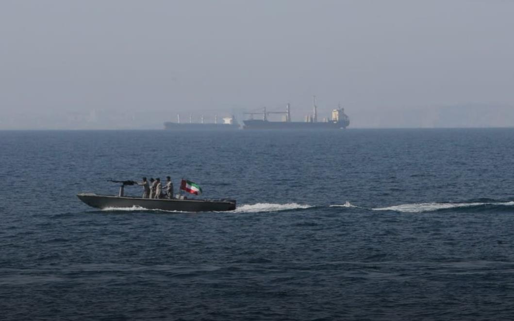 Small motorboat with several people and an Indian flag gliding over calm sea, a large cargo ship visible in the distance.