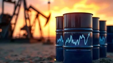 Oil barrels on a desert surface with a blue stock chart overlay showing rising prices at sunset in the background.