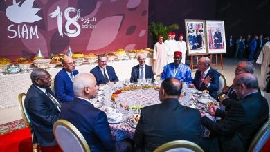 Group of men in suits seated around a round dining table at a formal event; banner reads 'SIAM 18 edition' in the background.