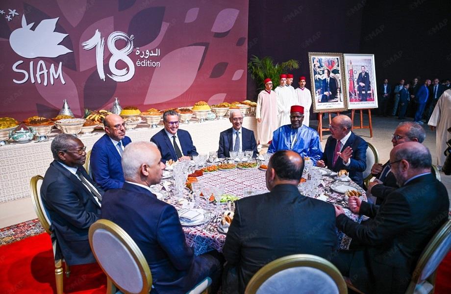 Group of men in suits seated around a round dining table at a formal event; banner reads 'SIAM 18 edition' in the background.