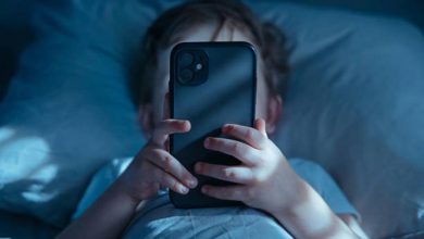Child lying in bed at night, holding a smartphone up to their face with blue-tinted light