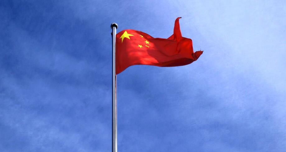 Red Chinese flag with yellow stars waving on a tall silver flagpole against a clear blue sky