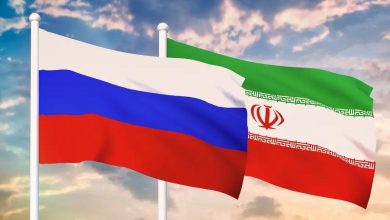 Russia and Iran national flags waving side by side against a cloudy sky on flagpoles.