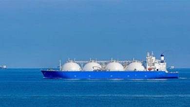 LNG carrier with four white spherical tanks sailing on calm blue sea, clear sky above.