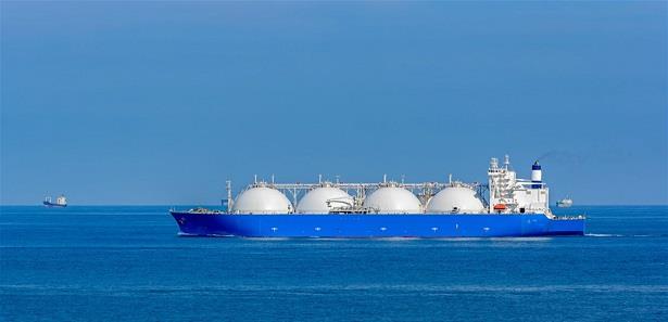 LNG carrier with four white spherical tanks sailing on calm blue sea, clear sky above.
