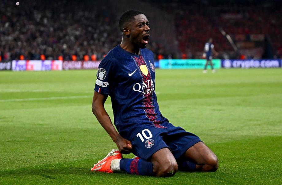 PSG soccer player kneels on the field, shouting in celebration, wearing a navy kit with Qatar Airways sponsor.