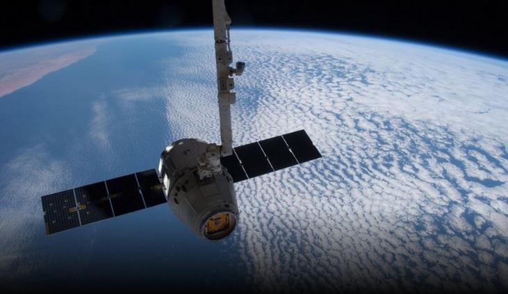Spacecraft with extended solar panels orbiting Earth, showing a blue curved horizon and cloud-covered planet below