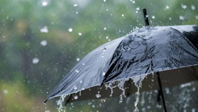 Black umbrella in heavy rain with droplets dripping from its canopy.