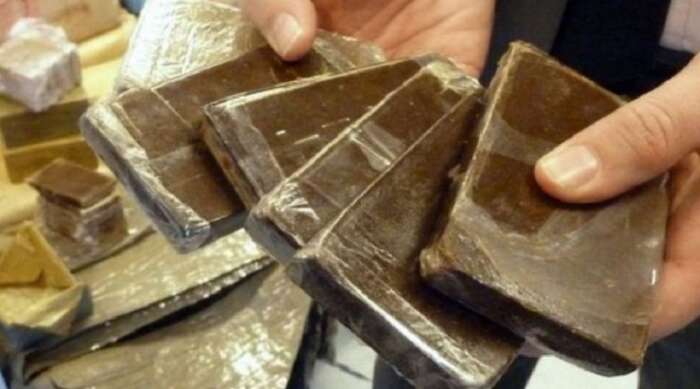 Close-up of dark chocolate chunks held between two hands, showing glossy surfaces and broken edges.