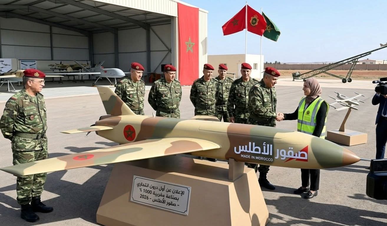 Moroccan military officers in camouflage and red berets gather around a large model missile labeled 'Made in Morocco' as a woman in a safety vest shakes hands with an officer.