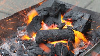 Glowing orange embers and black charcoal briquettes in a metal fire pit with sparks flying around.