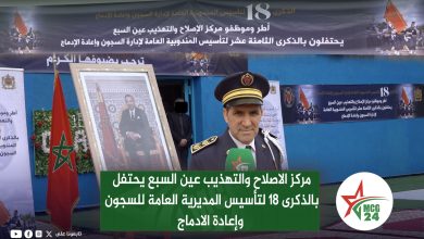 Moroccan officer in ceremonial uniform giving an interview beside a large portrait and flag, with banners commemorating the 18th anniversary of the penitentiary and reintegration administration.