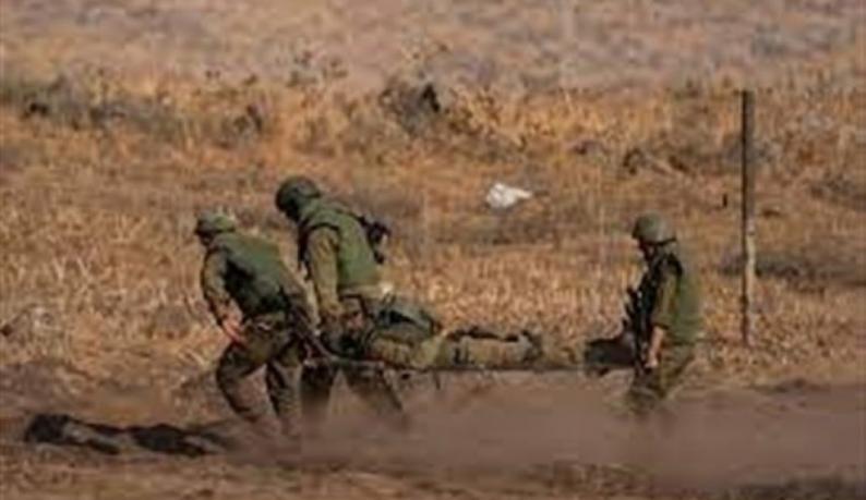Four soldiers in desert uniforms carry a wounded comrade on a stretcher across a dusty field.