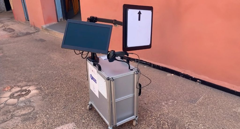 1000144961 | MCG24 | موقع إلكتروني مغربي شامل متجدد على مدار الساعة Portable wheeled kiosk with two screens mounted on a metal case; the right screen shows an upward arrow while the left screen is blank.