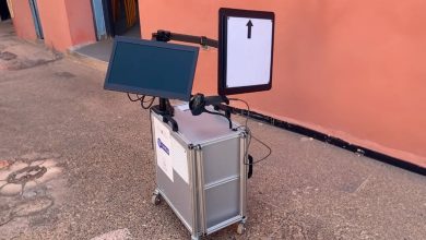1000144961 | MCG24 | موقع إلكتروني مغربي شامل متجدد على مدار الساعة Portable wheeled kiosk with two screens mounted on a metal case; the right screen shows an upward arrow while the left screen is blank.