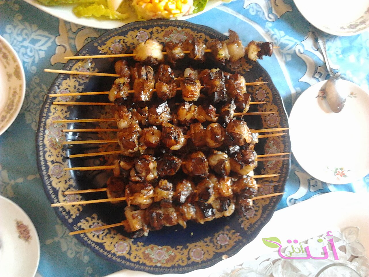 Skewers of grilled meat cubes arranged on a decorative blue plate at a dining table.
