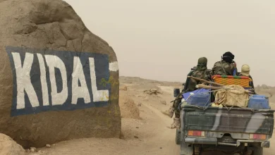 1512121jpeg | MCG24 | موقع إلكتروني مغربي شامل متجدد على مدار الساعة Desert road scene with a pickup truck carrying armed people in camo, driving past a large rock painted with the word 'KIDAL'.