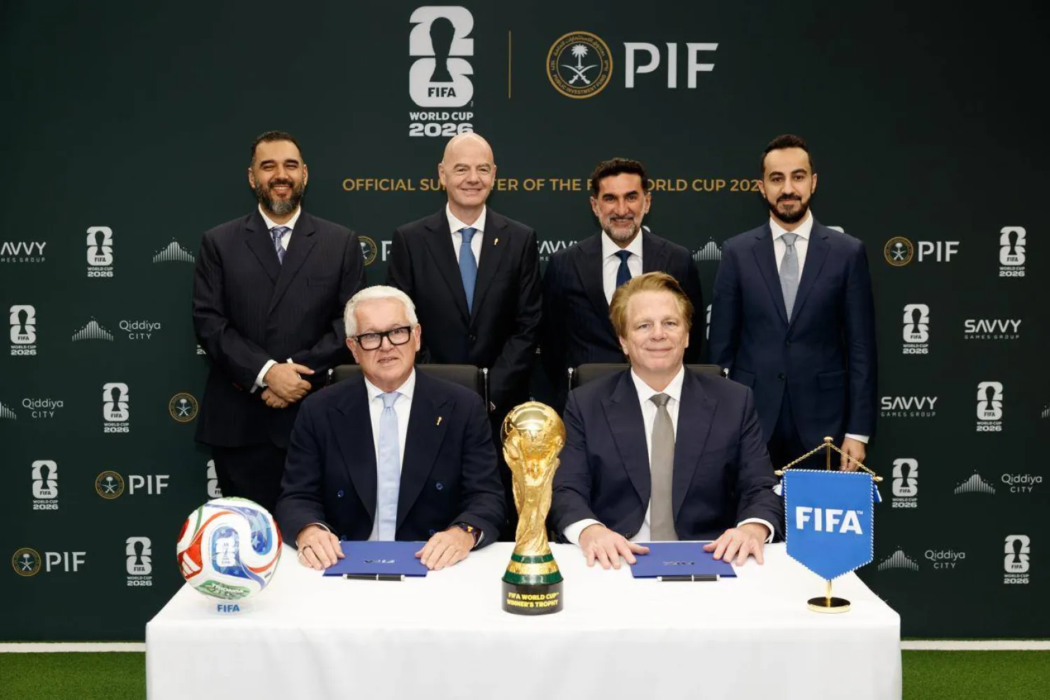 1541667jpeg | MCG24 | موقع إلكتروني مغربي شامل متجدد على مدار الساعة Six men in suits at a signing ceremony with the FIFA World Cup 2026 trophy on the table, ball to the left and a blue FIFA flag to the right.
