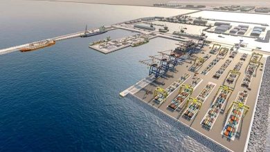 Aerial view of a large container port with stacked shipping containers, gantry cranes, and docked ships along the pier.