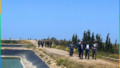 Group of people walking along a concrete water canal embankment beside a blue sky, sign for Société Régionale Multiservices L'Oriental SA visible overhead (Arabic and French).