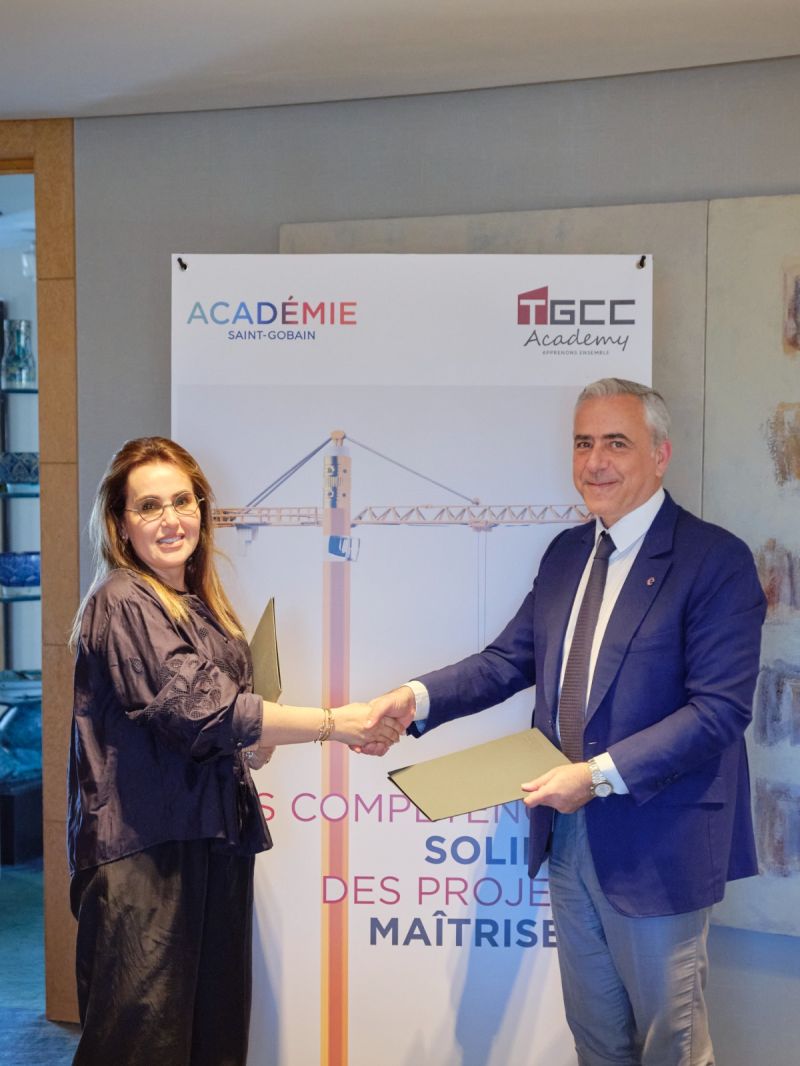 Two professionals shake hands in front of a banner reading Académie Saint-Gobain and TGEC Academy, signaling an agreement.