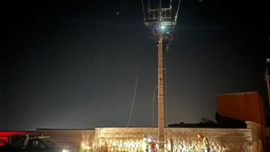 1779451762468 | MCG24 | موقع إلكتروني مغربي شامل متجدد على مدار الساعة Nighttime maintenance workers inspect a tall utility pole with power lines, near a wall and a car with headlights on
