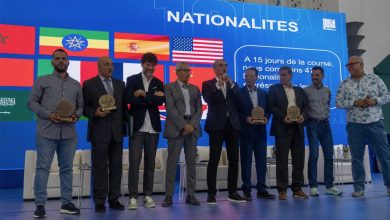 Group of men on a stage holding circular awards at an international event, with a blue backdrop displaying flags and the word NATIONALITES behind them.