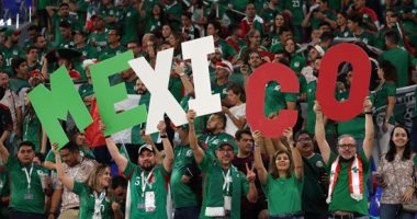 Group of Mexican soccer fans in green shirts cheering and holding large letters that spell MEXICO in a stadium crowd.