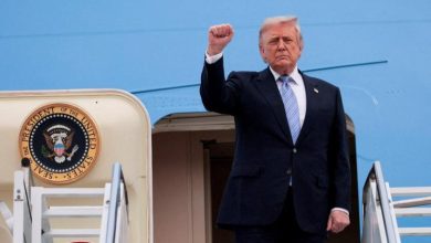 Former U.S. President Donald Trump raises his right fist while stepping down from Air Force One, with the presidential seal visible on the aircraft door.