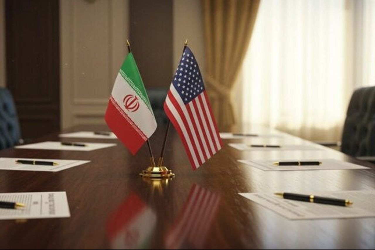 Diplomatic conference table with Iran and United States flags at center, papers and pens nearby
