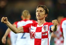 2332711 | MCG24 | موقع إلكتروني مغربي شامل متجدد على مدار الساعة Croatian footballer in a red-and-white checkered jersey celebrates with arms raised on the field, wearing number 10 cap and captain armband.",
