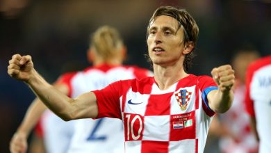 2332711 | MCG24 | موقع إلكتروني مغربي شامل متجدد على مدار الساعة Croatian footballer in a red-and-white checkered jersey celebrates with arms raised on the field, wearing number 10 cap and captain armband.",