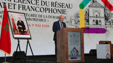 Man speaking at a podium during a conference on the network and Francophonie; Moroccan flag on the left and a framed portrait on an easel nearby.