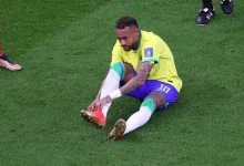 29538949 | MCG24 | موقع إلكتروني مغربي شامل متجدد على مدار الساعة Brazilian soccer player in a yellow kit sits on the grass and ties his red cleats during a match on a green field.