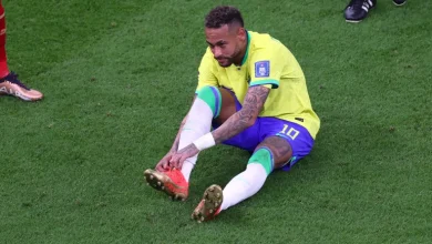 29538949 | MCG24 | موقع إلكتروني مغربي شامل متجدد على مدار الساعة Brazilian soccer player in a yellow kit sits on the grass and ties his red cleats during a match on a green field.