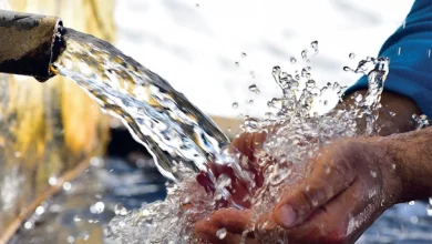 Hands cupping water flowing from a pipe, water splashing around them.