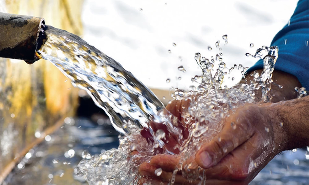 Hands cupping water flowing from a pipe, water splashing around them.