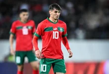 Soccer player in a red jersey with the number 10 and green shorts on a pitch during a match.
