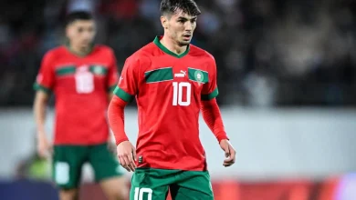 Soccer player in a red jersey with the number 10 and green shorts on a pitch during a match.