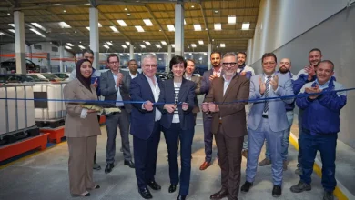 Group of professionals cutting a blue ribbon at a factory opening, with colleagues applauding in the background.