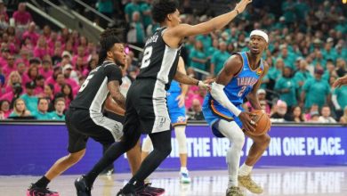 468184-696x464 | MCG24 | موقع إلكتروني مغربي شامل متجدد على مدار الساعة A basketball player in a teal Oklahoma City Thunder uniform dribbles the ball toward the basket while two defenders in black jerseys close in from the front, with a crowded arena in the background.